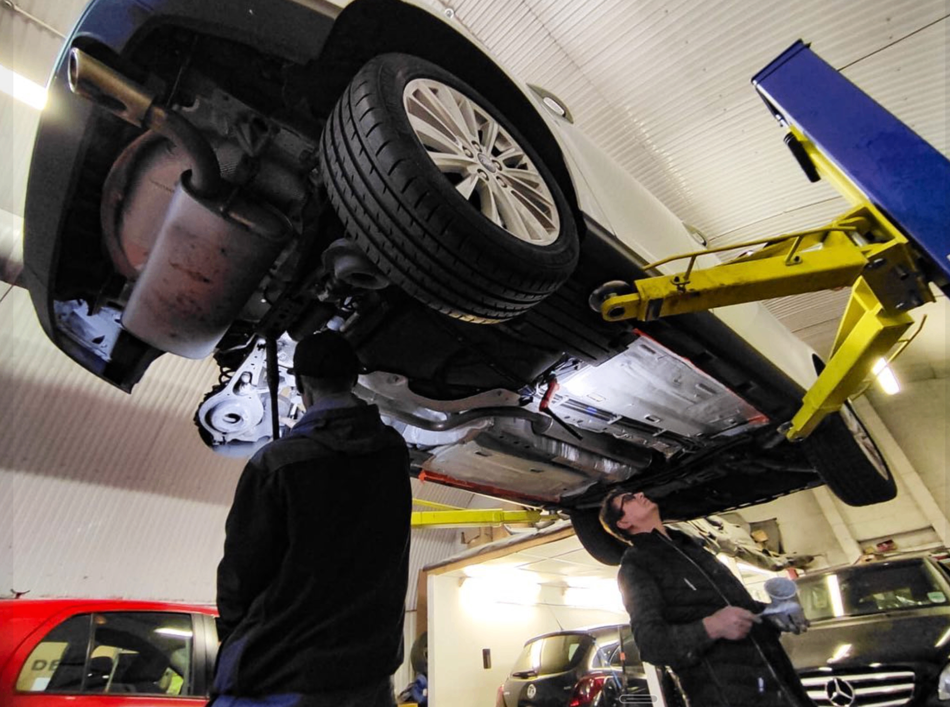 Two ADE technicians inspecting the underside of a customer car on the ramp